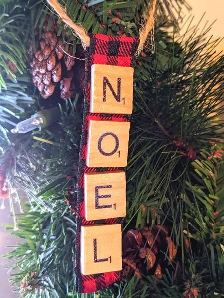 noel scrabble ornament hanging on greenery with pinecones