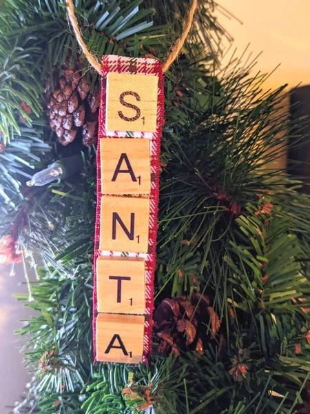 santa scrabble ornament hanging on greenery with pinecones